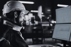Industrial engineer reviewing system data and performance metrics on multiple monitors in a production environment